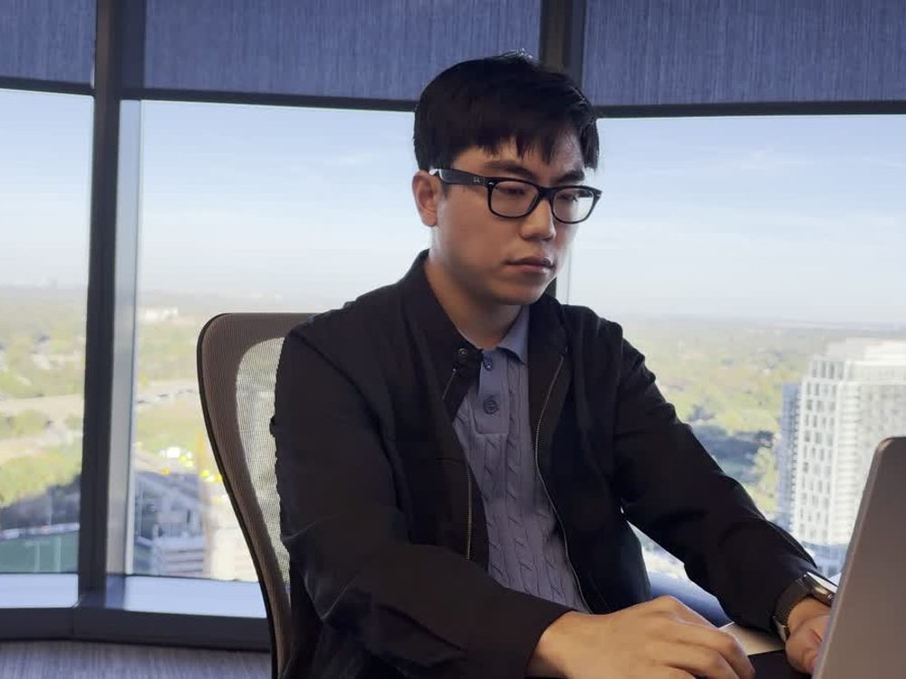Daniel at a laptop by a high-rise window.